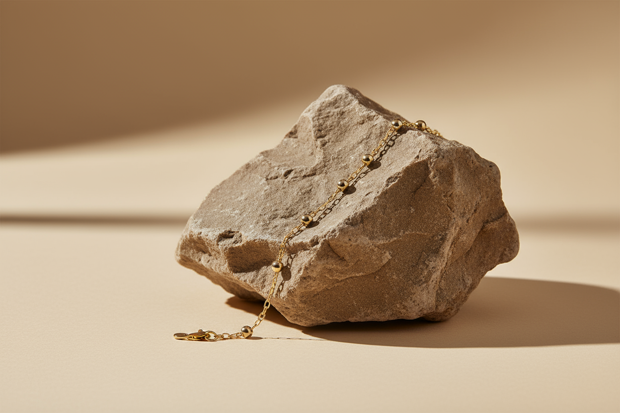 A rock on a crème beige background with shadow light on it . With a simple gold bracelet display on the rock 